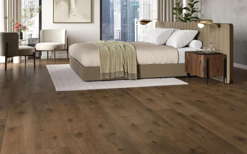 Schlafzimmer mit Bett und Sitzmöbeln auf dunklerem Holzlaminat