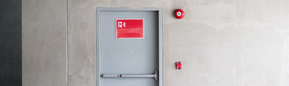 Feuerschutztür mit Sicherheitshinweis in einer Halle mit Feuermelder daneben 