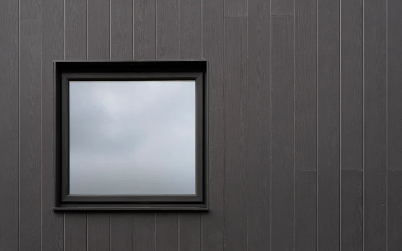Hausfassade mit schwarzen Fassadenplatten und einem kleinen Fenster
