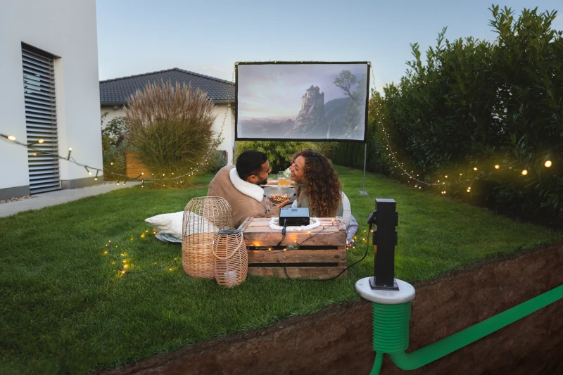 Pärchen liegt im Garten mit aufgebautem Video-Beamer und Leinwand 