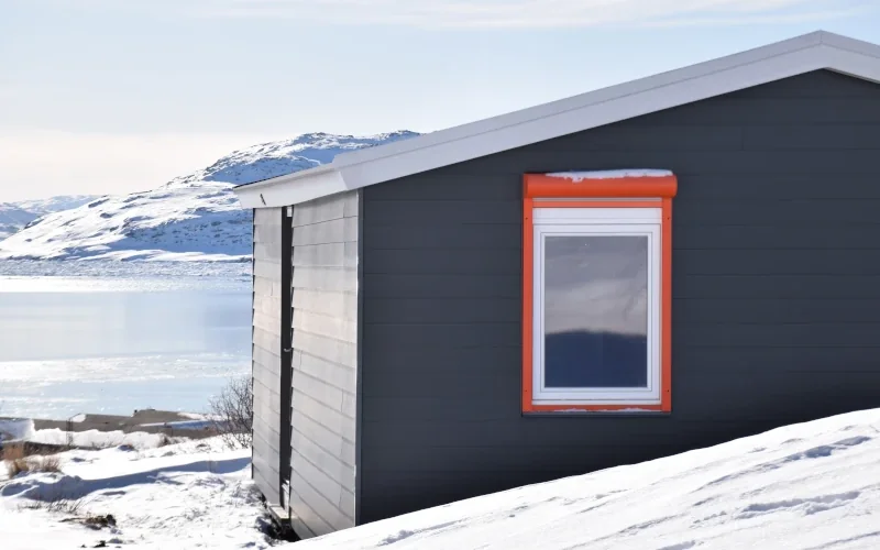 kleines Haus am See im Winter mit schwarzen Fassadenplatten