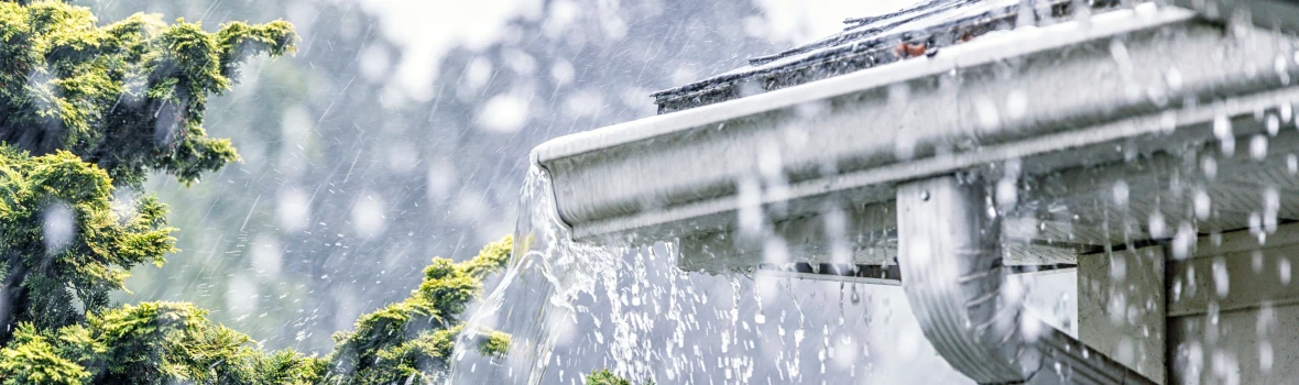 Regen prasselt auf ein Hausdach nieder und überschwemmt die Regenrinnen 