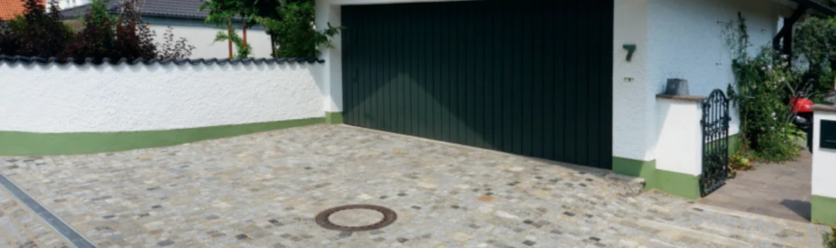 gepflasterte Hofeinfahrt mit Garage mit grünem Tor und einem Weg zum Haus