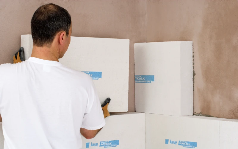 Das Bild zeigt einen Handwerker von hinten, der an einer Wand weiße Bauplatten montiert.