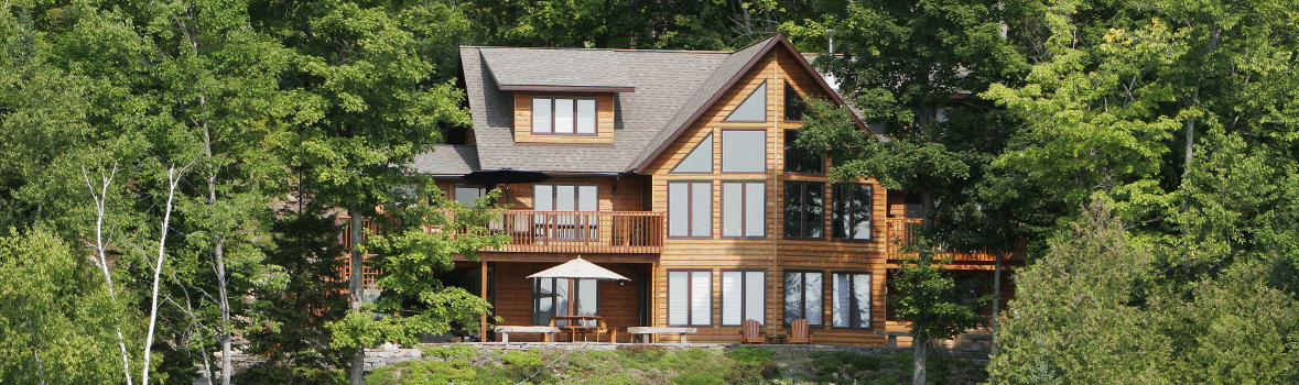 großes Holzhaus mit vielen Fenstern inmitten eines Laubwaldes