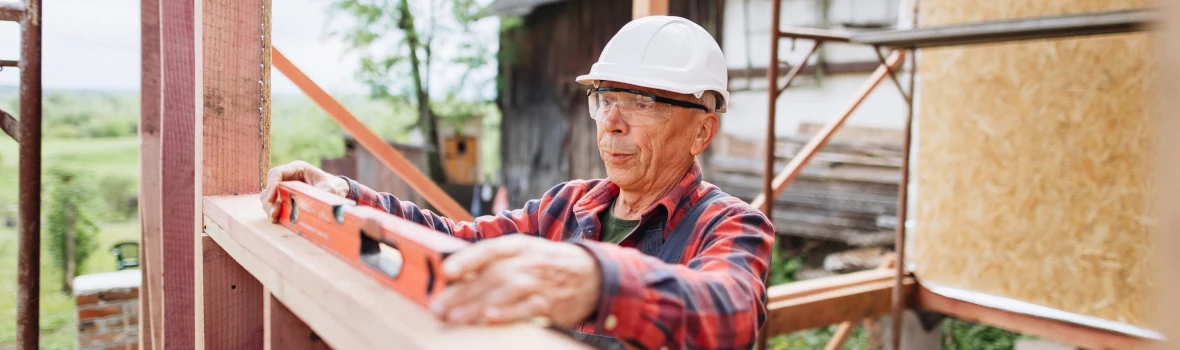 Ein alter Handwerker überprüft mit einer Wasserwaage ein Holzbau-Ständerwerk.