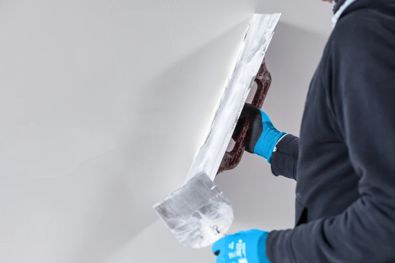 Handwerker trägt Putz auf weiße Wand mit Kelle auf.