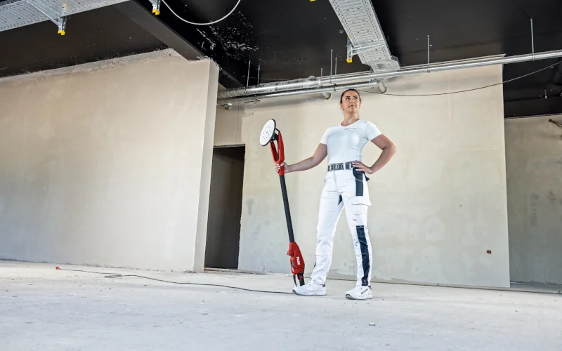 Malerin steht mit FLEX Wand- und Deckenschleifern in der Hand in einem Trockenbau
