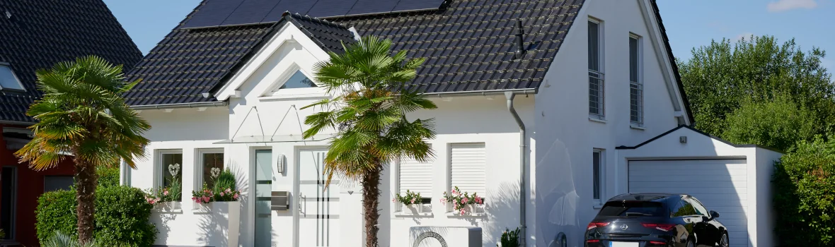 weißes Haus mit Vorgarten, Garage, Auto und Wärmepumpe an der Fassade