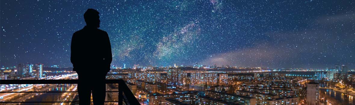 Mann steht auf einer Dachterrasse und guckt sich die Stadt an