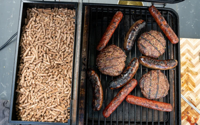 Pellet-Grill mit Pattys und Würstchen darauf