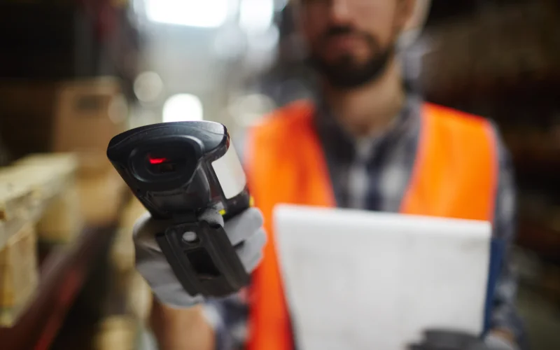 Lagermitarbeiter hält einen Scanner in die Kamera mit Dokumenten in der Hand