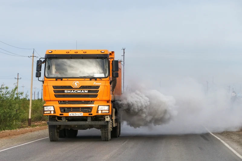 Eine orangener LKW mit Qualm hinter sich, auf eine Straße.