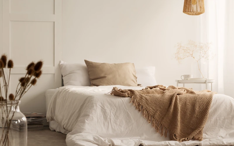 Gemütliches Schlafzimmer mit weißen Bett und Decke.