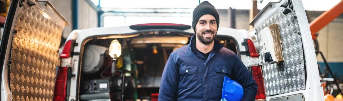 Handwerker steht vor eingeräumten Firmenfahrzeug mit geöffnetem Kofferraum