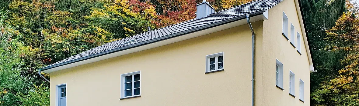 Umgeben von Bäumen steht ein Haus mit einer gelblich angestrichenen Fassade. 