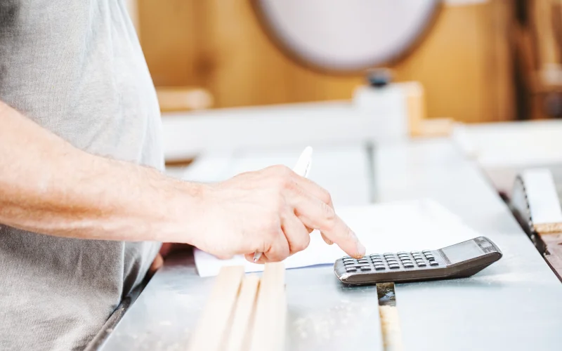 Handwerker steht in einer Werkstatt und rechnet etwas