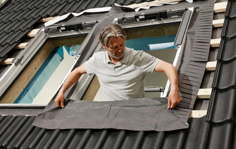 Handwerker baut Velux Zubehör in Dachfenster ein
