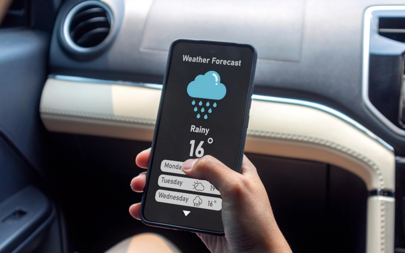 Hand einer Frau in einem Auto, die ein Mobiltelefon hält, um die Wettervorhersage zu überprüfen