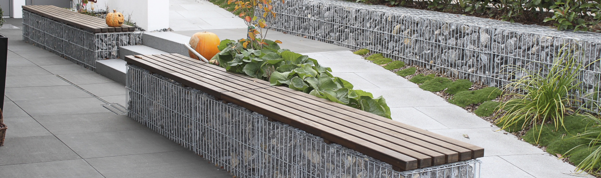 Drei Gabionen stehen auf einer Terrasse, zwei davon sind mit Holz als Sitzmöglichkeit.