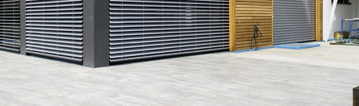 Modern gestalteter Terrassenbereich mit großformatigen Platten und verschatteter Glasfassade.