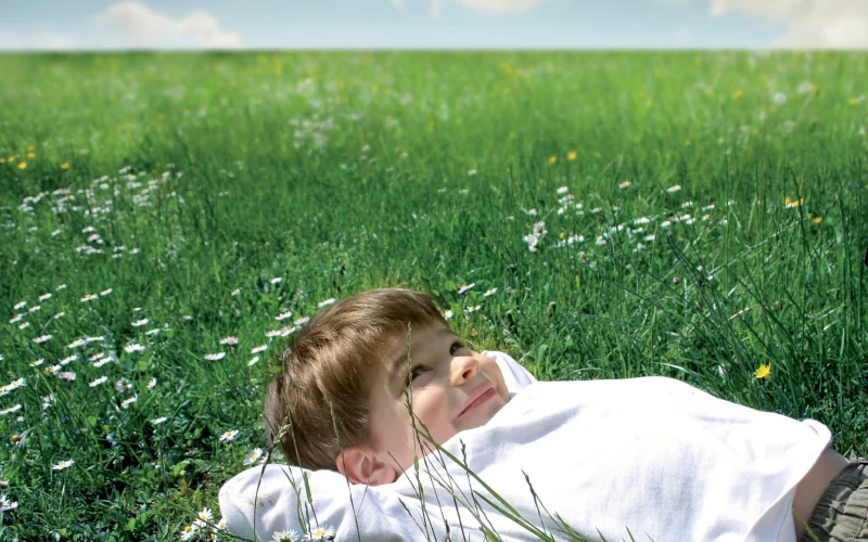 ein kleiner Junge liegt auf einer Wiese mit blauem Himmel