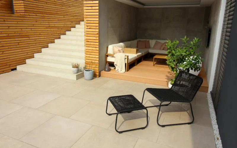 Terrasse mit Gartenstuhl und beigen Terrassenplatten und Treppenstufen und Sitzgruppe im Hintergrund