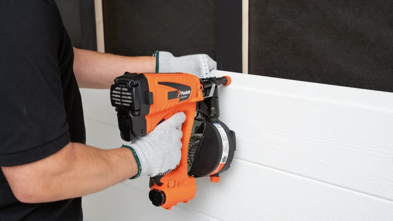 Handwerker bringt Fassadenplatten an Konstruktion am Haus mit spezieller Maschine an