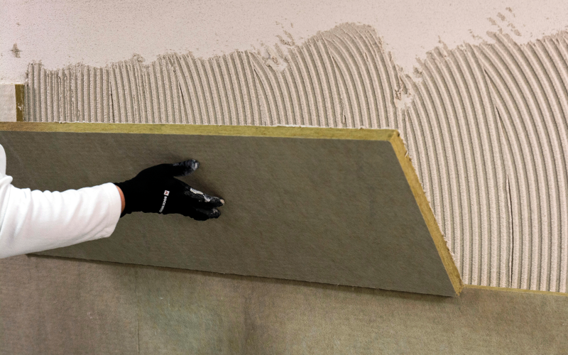 Eine Person drückt eine Dämmplatte auf eine mit Kleber bestrichene Wand.