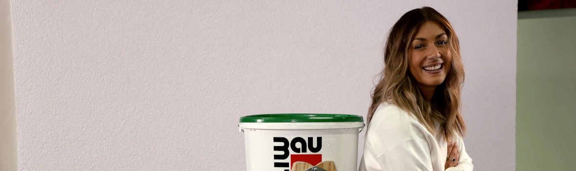 Frau lehnt sich an Leiter, auf dem ein baumit-Produkt steht. 