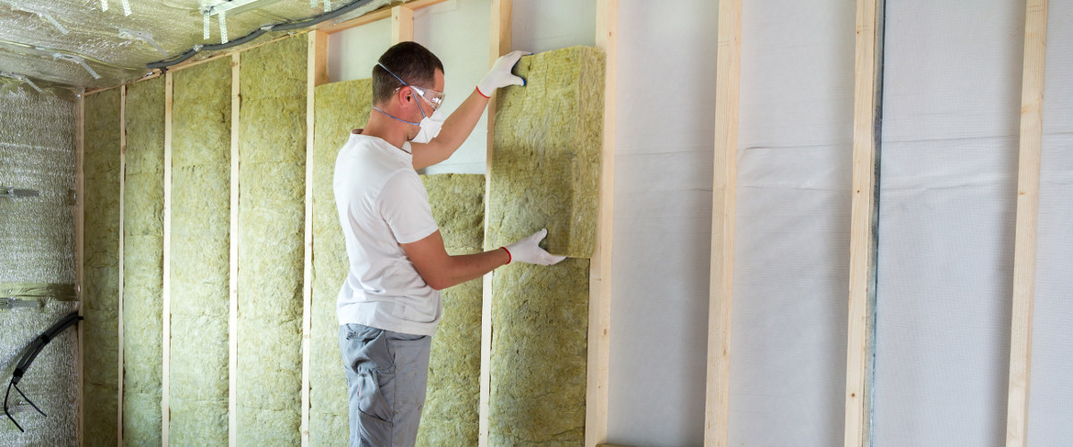 Arbeiter bringt Dämmplatten in Holzvorrichtung im Haus an