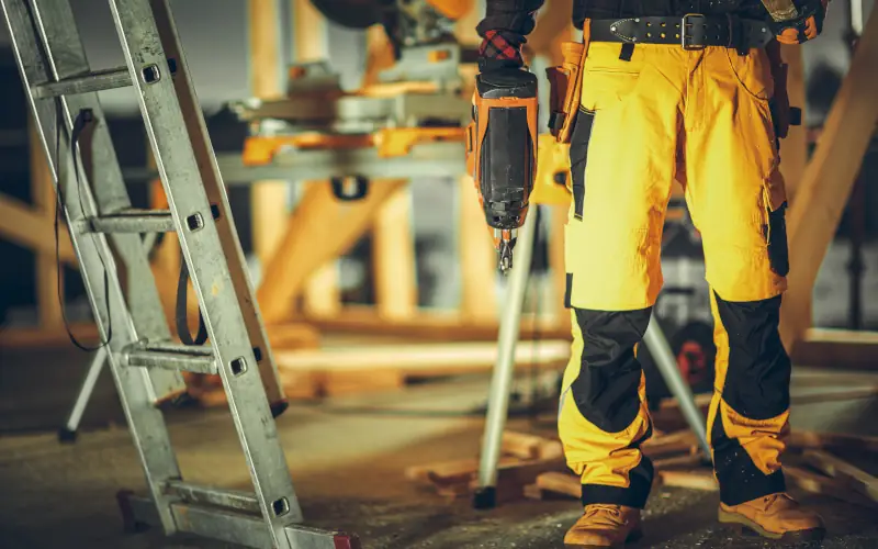 Handwerker steht auf einer Baustelle und hat Werkzeug in der Hand 