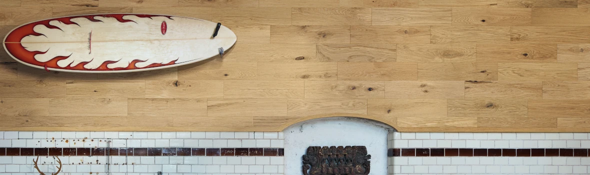 Wandpaneele aus Holz und darunter Fliesen. Auf den Holzpaneele ist ein Surfboard befestigt.