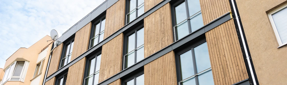 Blick von unten auf eine mit Holz und großen Fenstern sanierte Fassade an einem hohen Altbau.