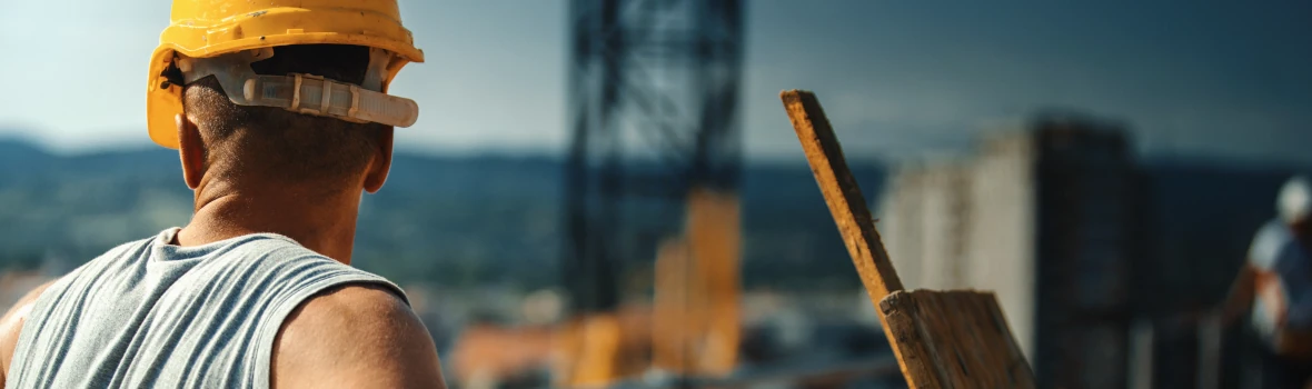 Handwerker steht auf einem Gerüst und schaut hinunter auf die Baustelle