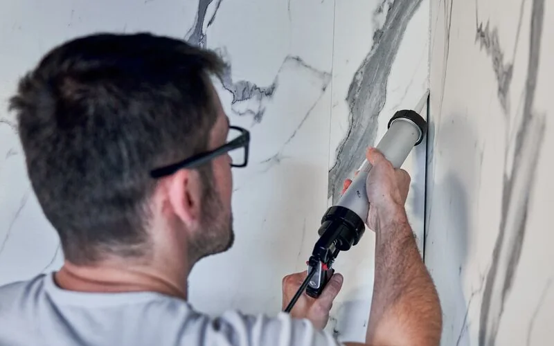 Handwerker versiegelt Wandpaneele mit Kleber