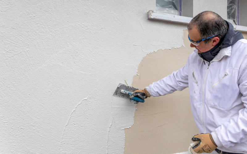 Ein Maler trägt mit einer Kelle Putz auf eine Wand auf.