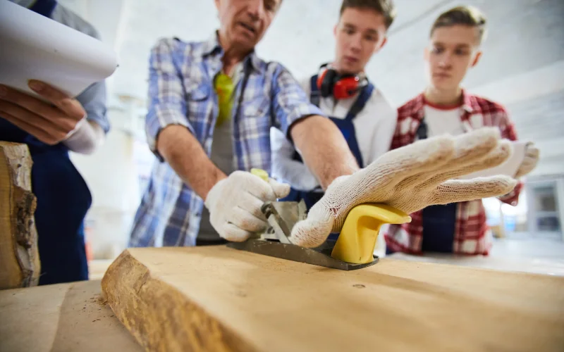 Tischler zeigt seinen Auszubildenden etwas in der Werkstatt