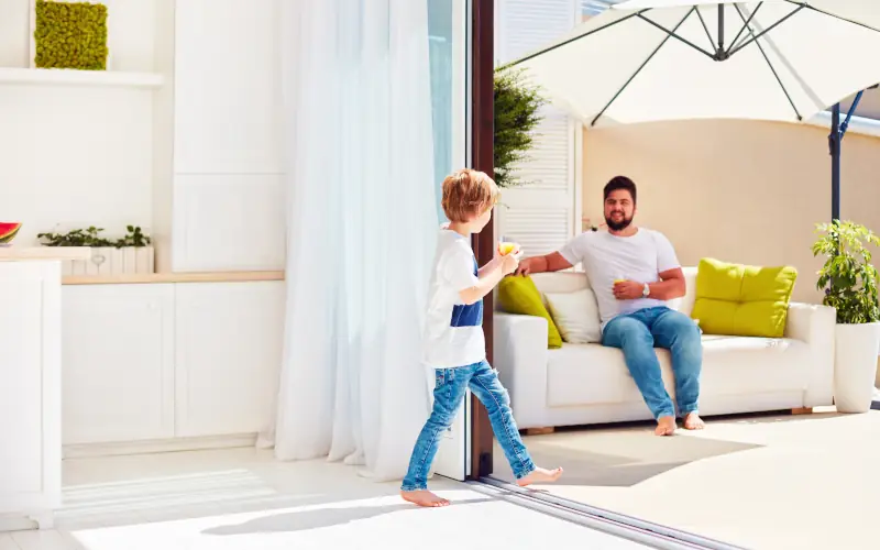 Kind geht auf die Terrasse auf der ein Vater auf einem Sofa wartet 