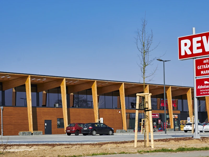 Moderner Supermarkt in Holzbauweise mit ansprechender Holzfassade und großen Fenstern.