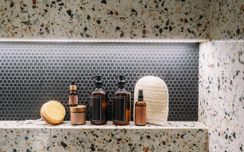 Bild eines Badezimmers: Ein Duschabsteller mit Terrazzo-Fliesenmuster, auf dem Duschgele und Seifen ordentlich verstaut sind.