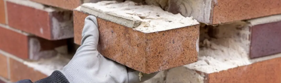 Ein rötlicher Ziegelstein mit Mörtel in einer Hand. 