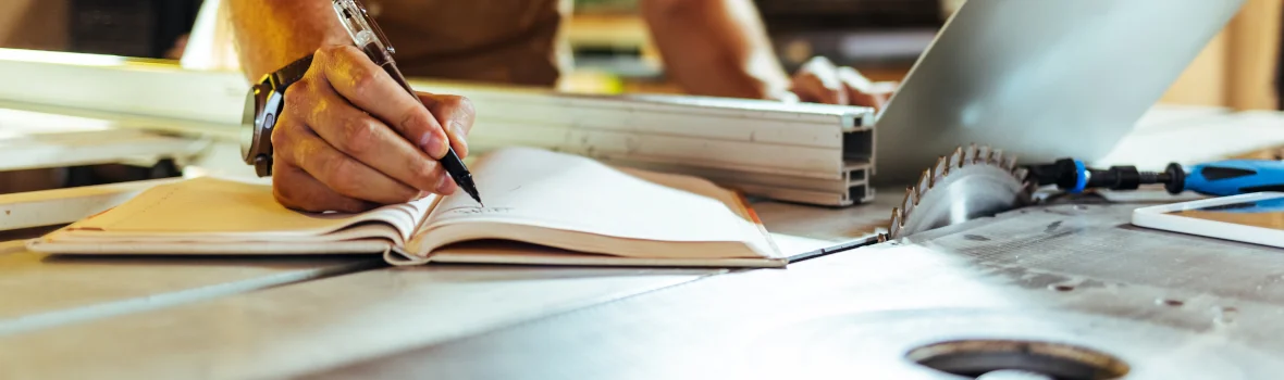 Handwerker mit Laptop schreibt etwas in ein Notizbuch