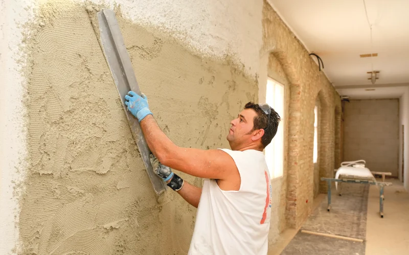 Handwerker verstreicht braune Masse mit einem Richtscheit an der Wand