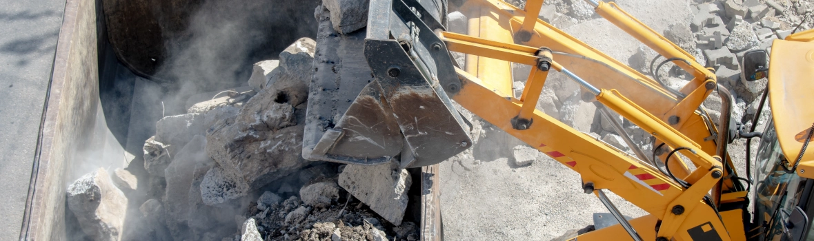 Bagger wirft mit seiner Schaufel Schutt in einen Container