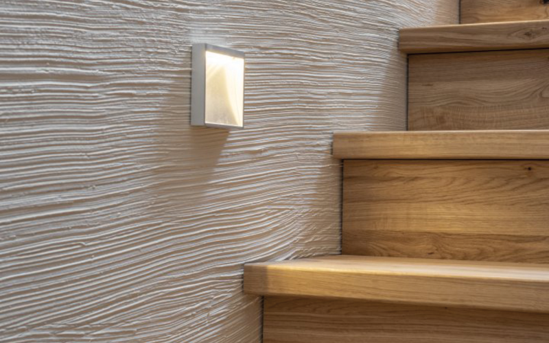 Holztreppe mit strukturierter Wand und eingebauter Wandleuchte.