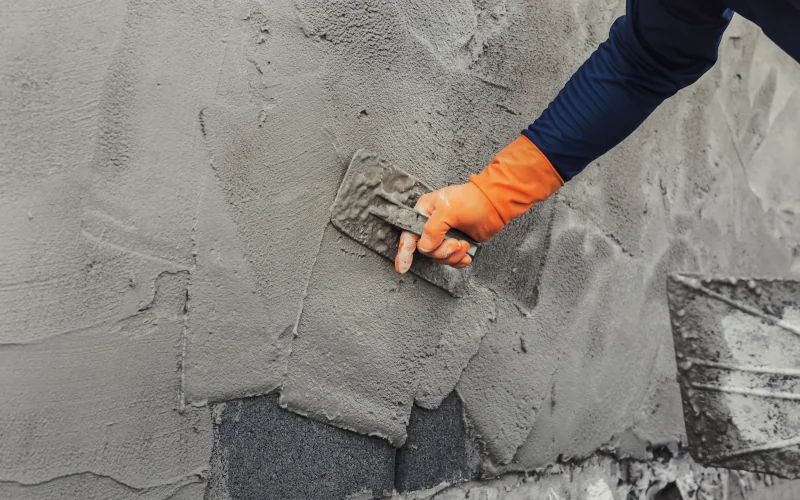 Handwerker mit Schutzhandschuhen bringt Putz an Hauswand an 