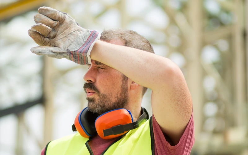 Handwerker wischt sich das Gesicht bei Arbeit in der Sommerhitze 