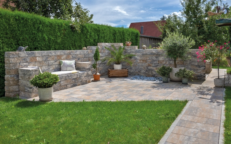 Gartenmauer der Marke KANN mit Terrassenmöbeln und Rasenfläche.