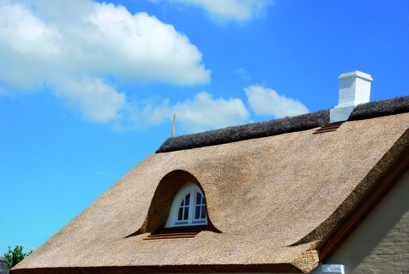 Ein traditionelles Reetdachhaus unter blauem Himmel mit weißen Wolken.